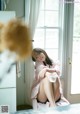 A woman sitting on a bed in front of a window.