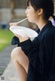 A woman sitting on a bench eating a plate with chopsticks.