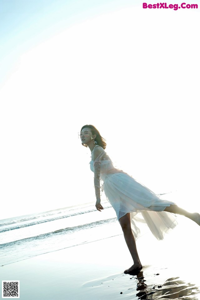 A woman in a white dress is walking on the beach.