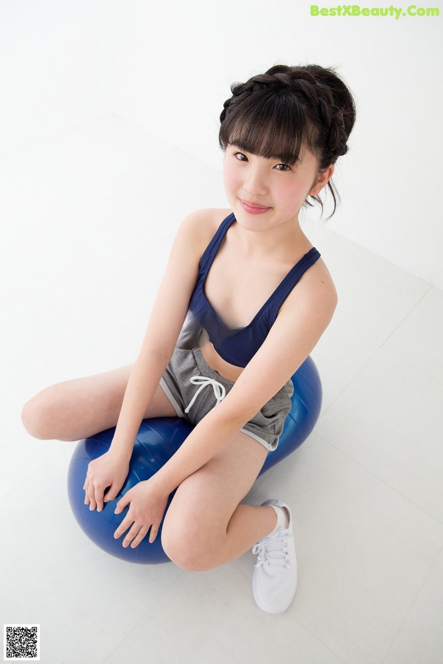 A woman sitting on a blue ball on a white floor.
